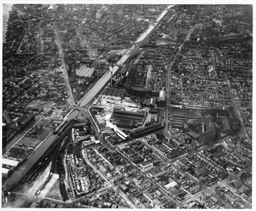 The impact of the Delaware and Raritan Canal on the City of Trenton is often difficult to recognize today, since a sizeable portion of the main canal was filled and replaced by a network of highways and the River Line light rail system in the 20th century.  However, the canal had a substantial impact on the industrial growth of the City of Trenton.  The city’s location at the head of navigation on the Delaware River had already proved an advantage to its economy; but, the canal provided Trenton with an additional benefit by creating a direct inland water link to the Raritan Bay and the cities of the eastern seaboard beyond.  This aerial photograph, taken in April of 1930, shows how prominent a feature the canal was in Trenton, and the many manufacturing facilities and potteries that flourished in the State Capital in the 19th and 20th centuries.  (Photograph reproduced courtesy of the Hagley Museum and Library https://www.hagley.org/research/search-hagley-collections ) 